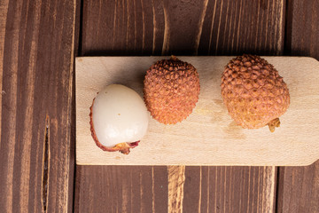 Wall Mural - Group of three whole fresh lychee on wooden cutting board flatlay on brown wood