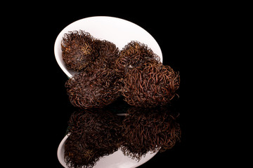 Wall Mural - Lot of whole dark old brown rambutan with blue chinese ceramic bowl isolated on black glass