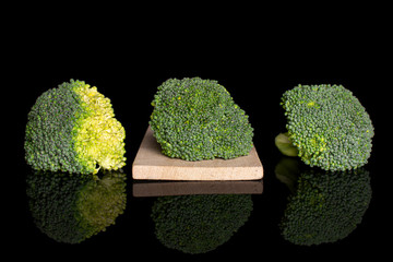 Sticker - Group of three whole fresh green broccoli head on small wooden cutting board isolated on black glass