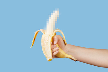 Hidden censored banana in hand on a blue background. Horny (aroused) penis, male erection and sexual education. Funny pornography.