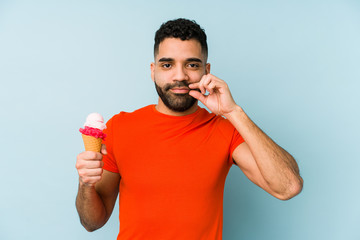 Wall Mural - Young latin man holding an ice cream isolated with fingers on lips keeping a secret.