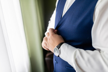 Wall Mural - Man in a white shirt and a blue vest is buttoning a vest. A stylishly dressed businessman adjusts the buttons on his vest.