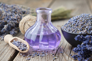 Wall Mural - Bottle of essential lavender oil or infused lavender flowers water and bowl of dry lavender petals on wooden table.