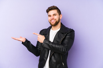 Canvas Print - Young man isolated on purple background excited holding a copy space on palm.