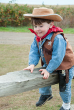Toddler Dressed As A Cowboy Sitting On A Fence Post.