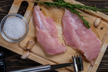 Fresh raw chicken breast on a board with spices and herbs on a wooden table