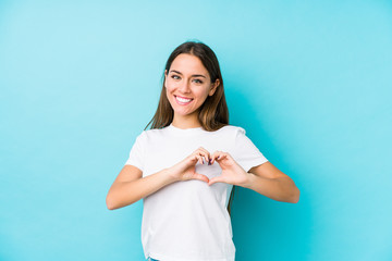 Wall Mural - Young caucasian woman  isolated smiling and showing a heart shape with hands.