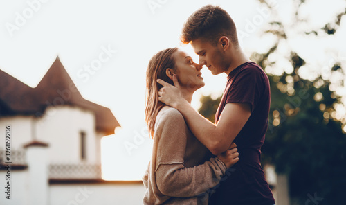 Caucasian couple kissing each other in front of the sunset embracing and having Poster Mural XXL