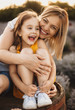 © Strelciuc - Caucasian girl sitting near her mother on a barrel while smiling and embracing each other during a sunny evening
