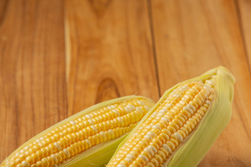 Two pieces of corn placed on a wooden background.