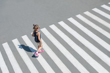 Stylish Child In Sun Glasses, Fashion Clothes Walking Along Summer City Crosswalk. Kid On Pedestrian Side Walk. Concept Pedestrians Passing A Crosswalk. From Top View. Behind. Shadow At Zebra Crossing
