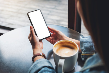 mockup image of a woman holding black mobile phone with blank white screen with coffee cup on the ta