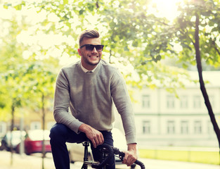 Wall Mural - lifestyle, transport and people concept - happy smiling young man in sunglasses riding bicycle on city street