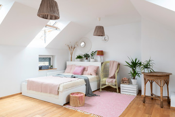 Wall Mural - Interior of white bedroom in the attic with double bed and pink decoration. Cozy room in apartment with wooden floor, carpet, armchair and table. Bright indoors with window.