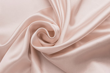 Smooth wrinkled silk bedsheet, fabric background. Abstract crumpled satin texture. Cream color. Folded cloth, wallpaper. Soft wavy pastel beige material, pink glossy textile.