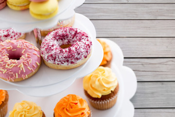 Wall Mural - fast food, dessert and sweets concept - close up of glazed donuts and cupcakes on stand over grey wooden boards background