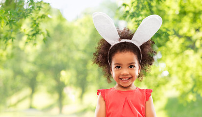 Wall Mural - easter, holidays and childhood concept - happy little african american girl wearing bunny ears headband over green natural background