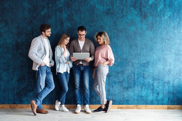 The connected team is an efficient team. Group of businesspeople using wireless technology together while standing in line against a blue background.