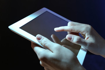 Woman using tablet on dark background, closeup
