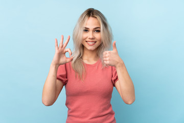 Teenager girl over isolated blue background showing ok sign and thumb up gesture