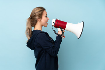 Teenager Russian girl holding mat isolated on blue background shouting through a megaphone