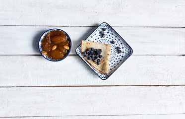 Pancake with blueberries in plate, apricot jam with nuts in bowl  on white wooden background