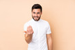 © luismolinero - Caucasian handsome man isolated on beige background inviting to come with hand. Happy that you came