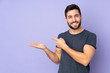 © luismolinero - Caucasian handsome man holding copyspace imaginary on the palm to insert an ad over isolated purple background