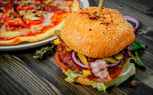 Bacon Cheese Burger With Beef Patty Tomato Onion And Pizza On A Wooden Table