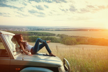 Attractive Yong Woman Is Lying On The Car's Hood And Looking At Sunset. Rural Evening Background.
