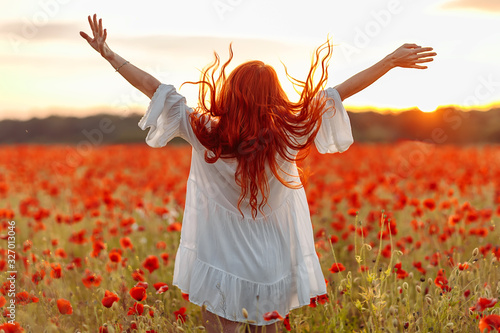 Fotomural Happy redhead smiling woman in white dress on field of poppies at summer sunset