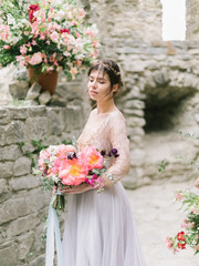 Portrait of a tender young bride. Beautiful sensual young brunette bride in long wedding dress holding colorful bouquet outdoor. Fine art photography 