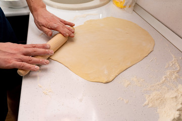 Roll out the dough. baker rolls out the dough on a wooden kitchen table sprinkled with flour