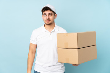 Wall Mural - Delivery caucasian man isolated on blue background standing and looking to the side