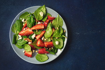 Wall Mural - Close up of a plate with strawberry and spinach salad on blue background