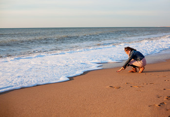 Pretty woman walking on the sand beach, the wind blowing hair of the model. Woman enjoing the waves on the ocean and breathing fresh air at sunset