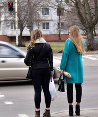 two blond girls are standing in front of a pedestrian crossing and waiting for a green traffic light