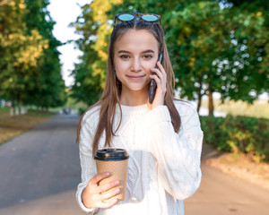happy girl smiles rejoices, teenager 12 years old, phoning smartphone hand, cup coffee tea, listenin