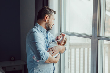 Middle age Caucasian father trying to calm down newborn baby. Man parent holding rocking a child on his hands. Authentic lifestyle family moment. Single dad home life concept.