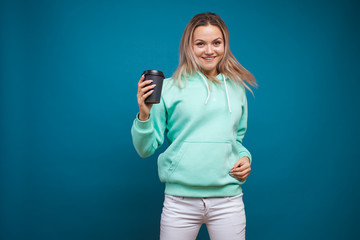 Wall Mural - Happy girl smiling and drinking coffee, portrait in Studio on blue background.