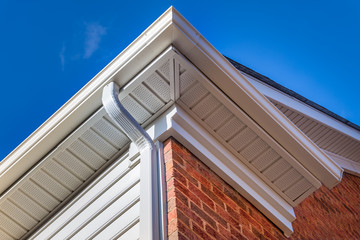 Wall Mural - Close up of white frame gutter guard system, eaves through, fascia, drip edge, colonial white soffit with ventilation, brick facade siding on a luxury American single family home neighborhood USA