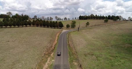 Poster - Bending road in scenic green valley with cattle farms in Australian Blue Mountains with convertible car driving uphill.