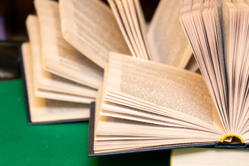 Vintage old book open in a library on an old green carved table with gold encyclopedia books in the background