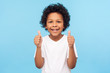 © khosrork - Like! Portrait of happy little boy with curly hair in white T-shirt smiling at camera and doing thumbs up gesture, showing agree cool approval sign. indoor studio shot isolated on blue background