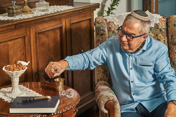 Senior Jew in armchair drinks wine in traditional home 