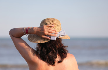 Wall Mural - woman waiting with hand on the straw hat in summer