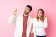 © luismolinero - Couple in Valentine Day over isolated pink background with fingers crossing and wishing the best