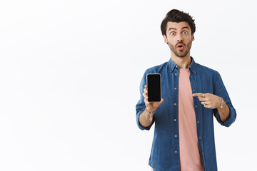 Wall Mural - Man found excellent online shop to buy gifts, pointing smartphone and telling it must have. Excited happy handsome bearded guy showing something on mobile screen with pleased expression