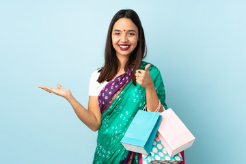 Young Indian woman with shopping bags holding copyspace imaginary on the palm to insert an ad and with thumbs up