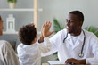 © fizkes - Smiling African American doctor giving high five to little boy